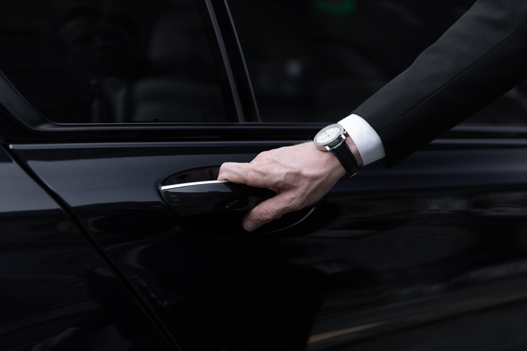 Chauffeur's hand opening the rear door of a black BMW 7 Series