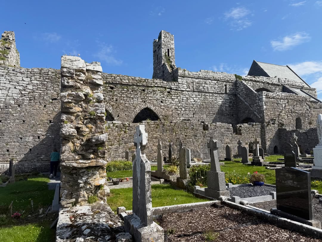 The ruined stone walls and graveyard of Corcomroe Abbey under a clear sky